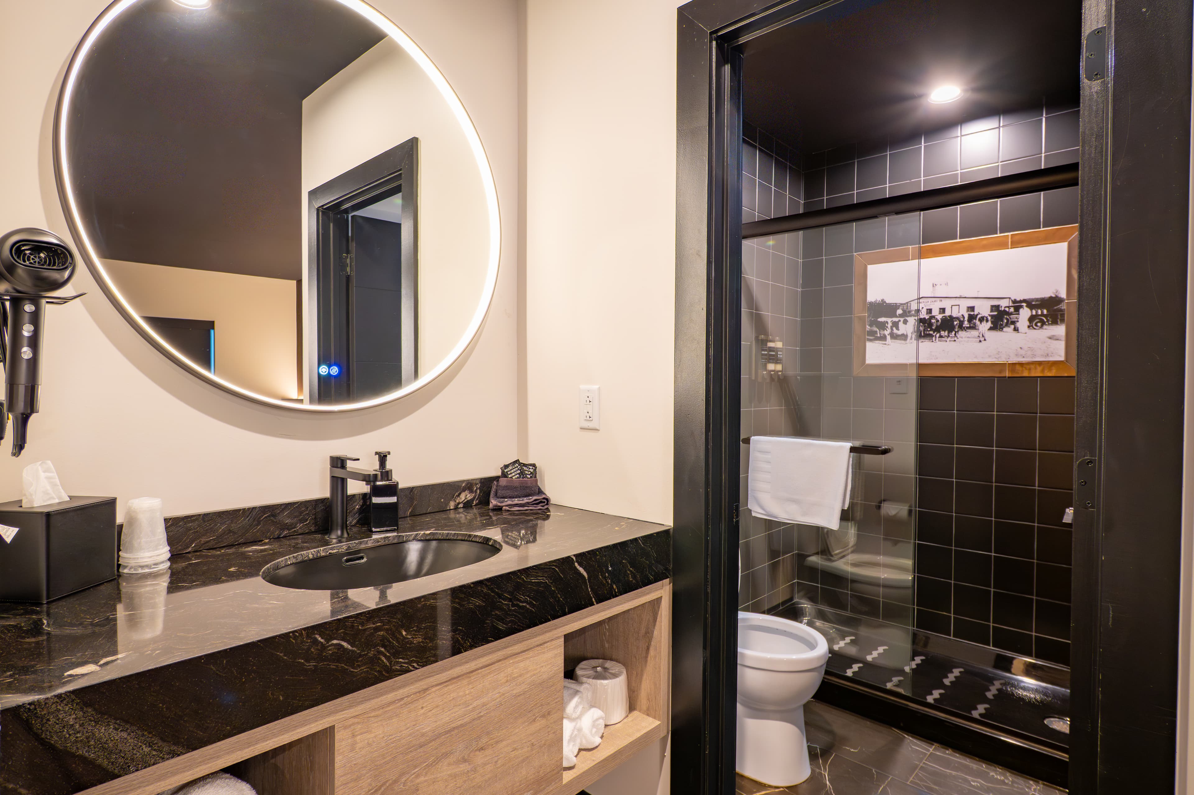Modern bathroom featuring a round mirror, sleek black tiles, and a glass shower enclosure.