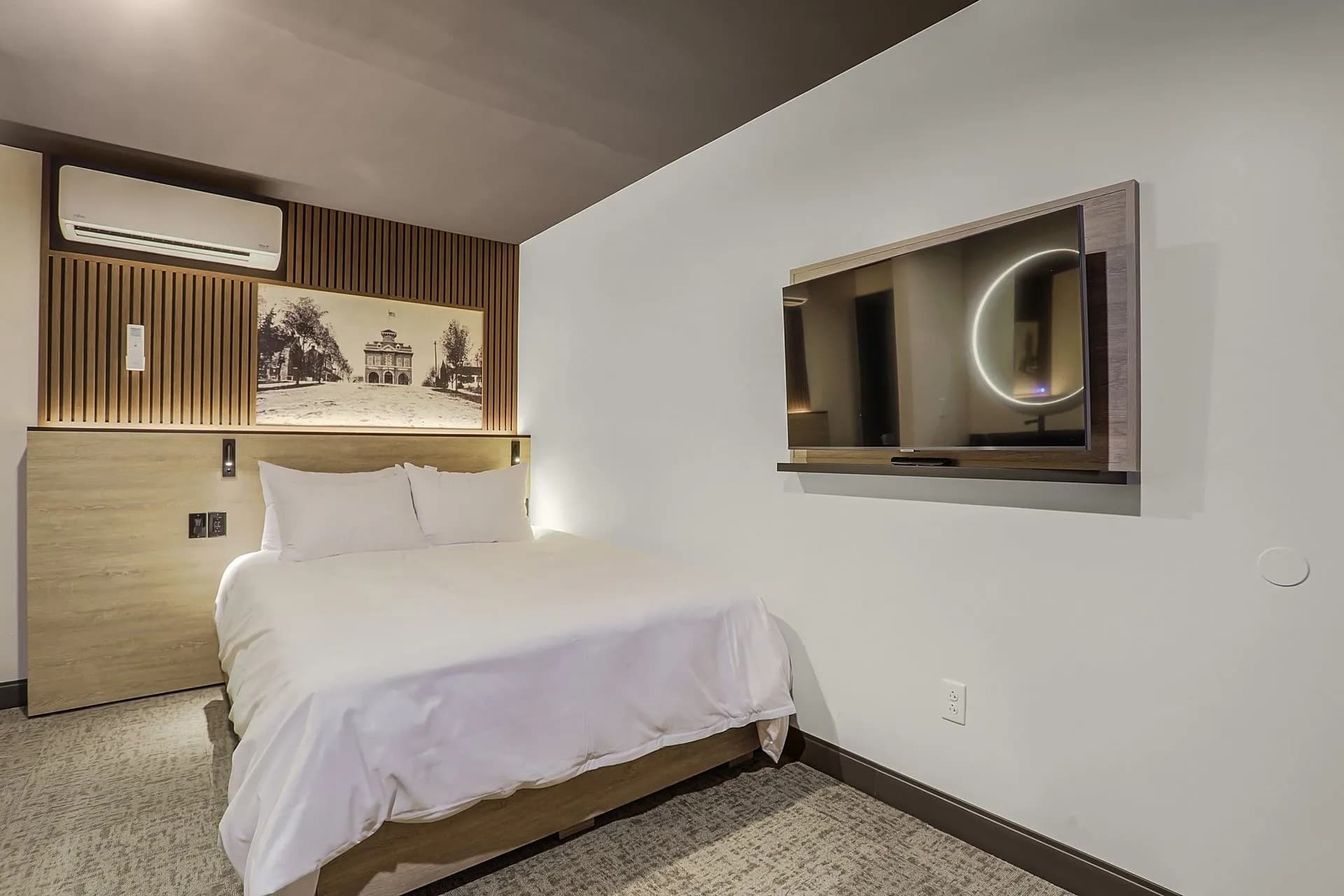 A cozy hotel room featuring a bed, air conditioner, and mounted television.