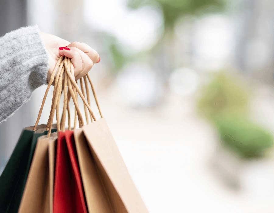 A hand holding multiple shopping bags in a blurred outdoor setting.