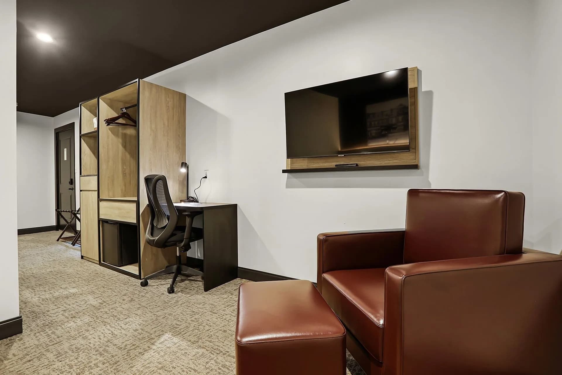A modern hotel room featuring a seating area, desk, and mounted television.