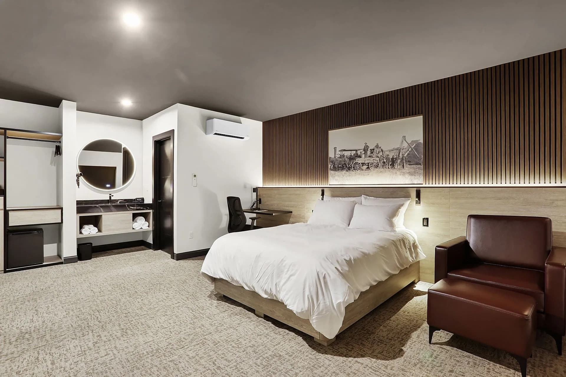 Modern hotel room featuring a bed, desk, and seating area with minimalist decor.