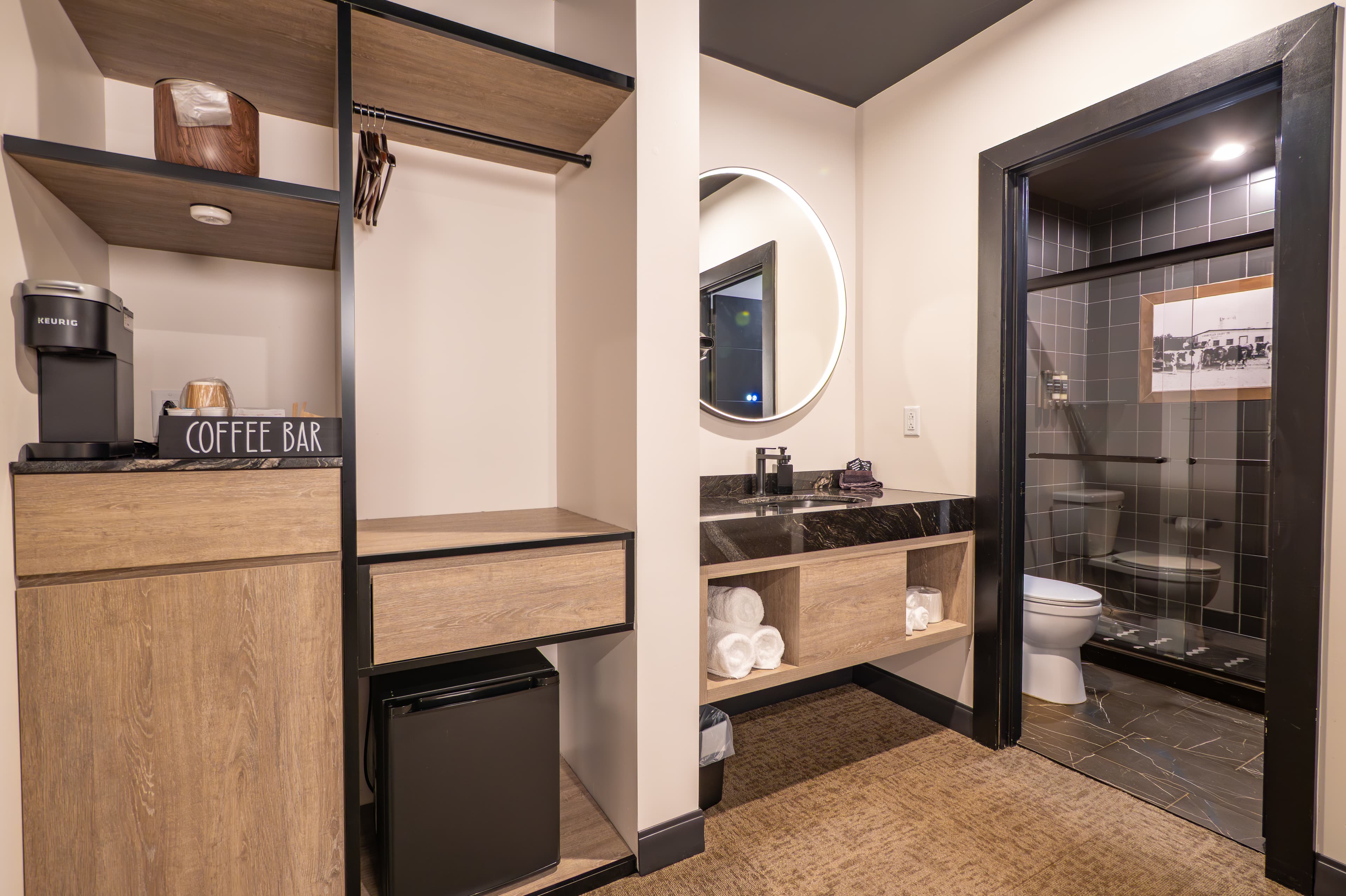 A modern hotel room featuring a coffee bar, storage, and a bathroom with a shower.