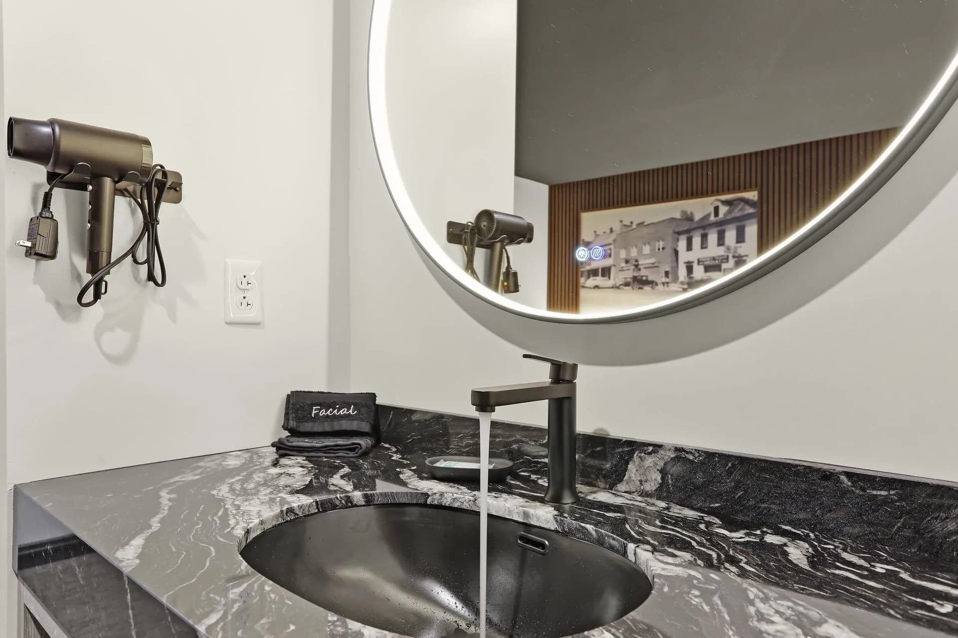 A modern bathroom sink with a black marble countertop, faucet, mirror, and hair dryer.