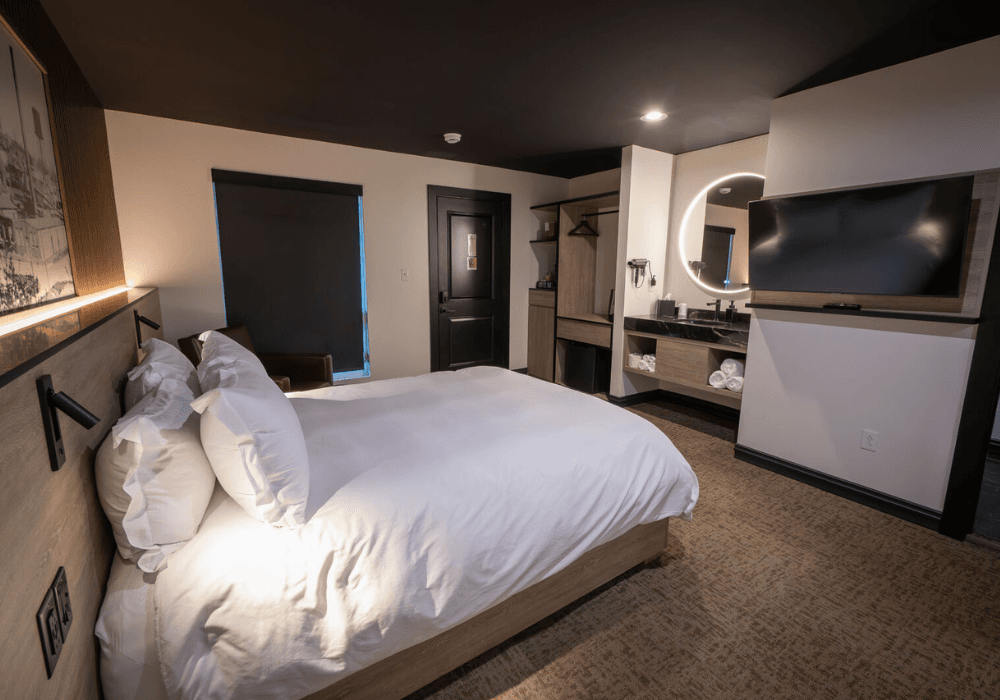 A modern hotel room featuring a queen bed, wall-mounted TV, and stylish furnishings.