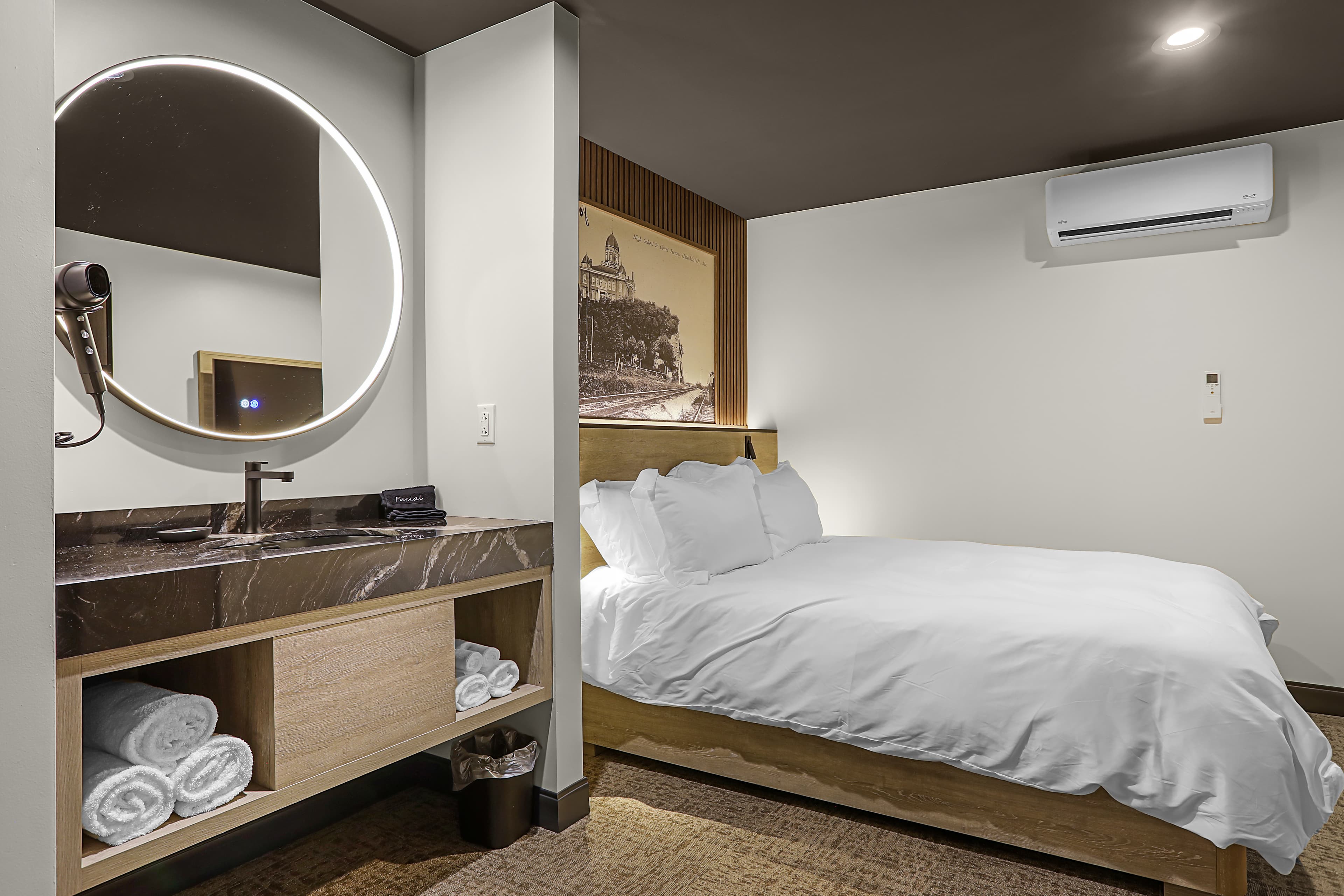 A modern hotel room featuring a bed, a circular mirror above a sink, and a minimalist design.
