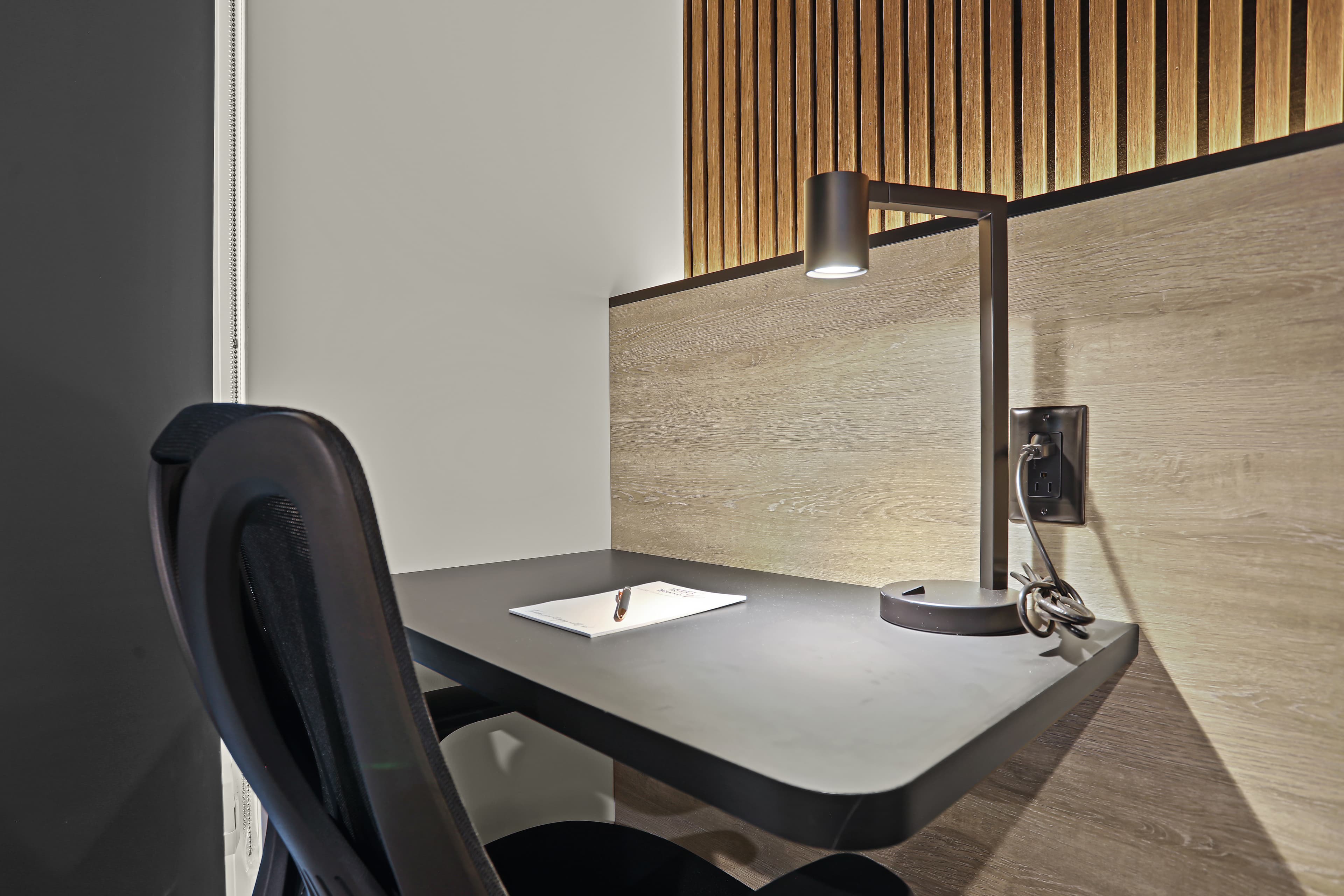 A modern desk with a lamp and a chair, set against a wooden wall.
