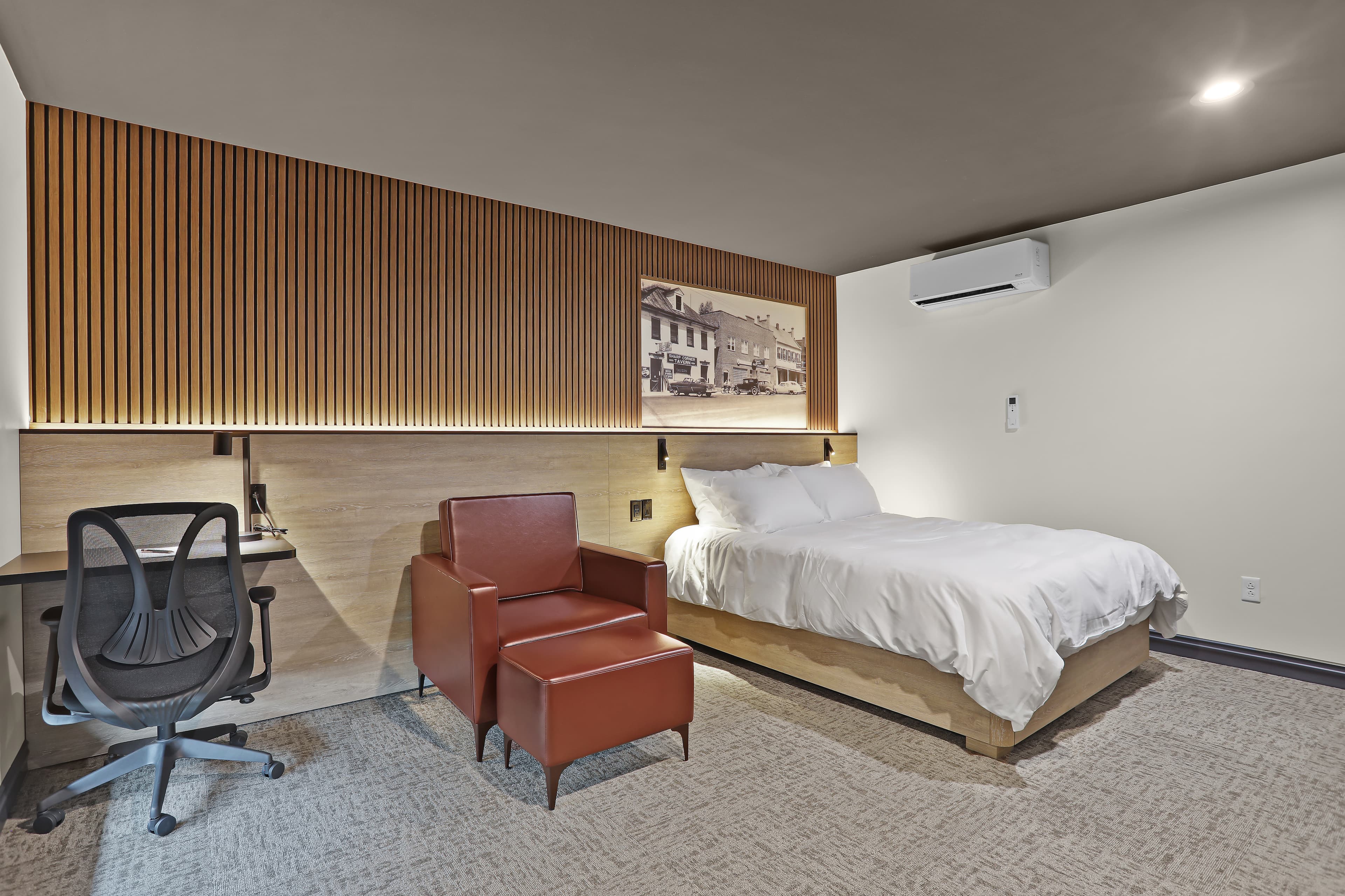 A modern hotel room featuring a bed, a red chair, and a desk against a wooden accent wall.