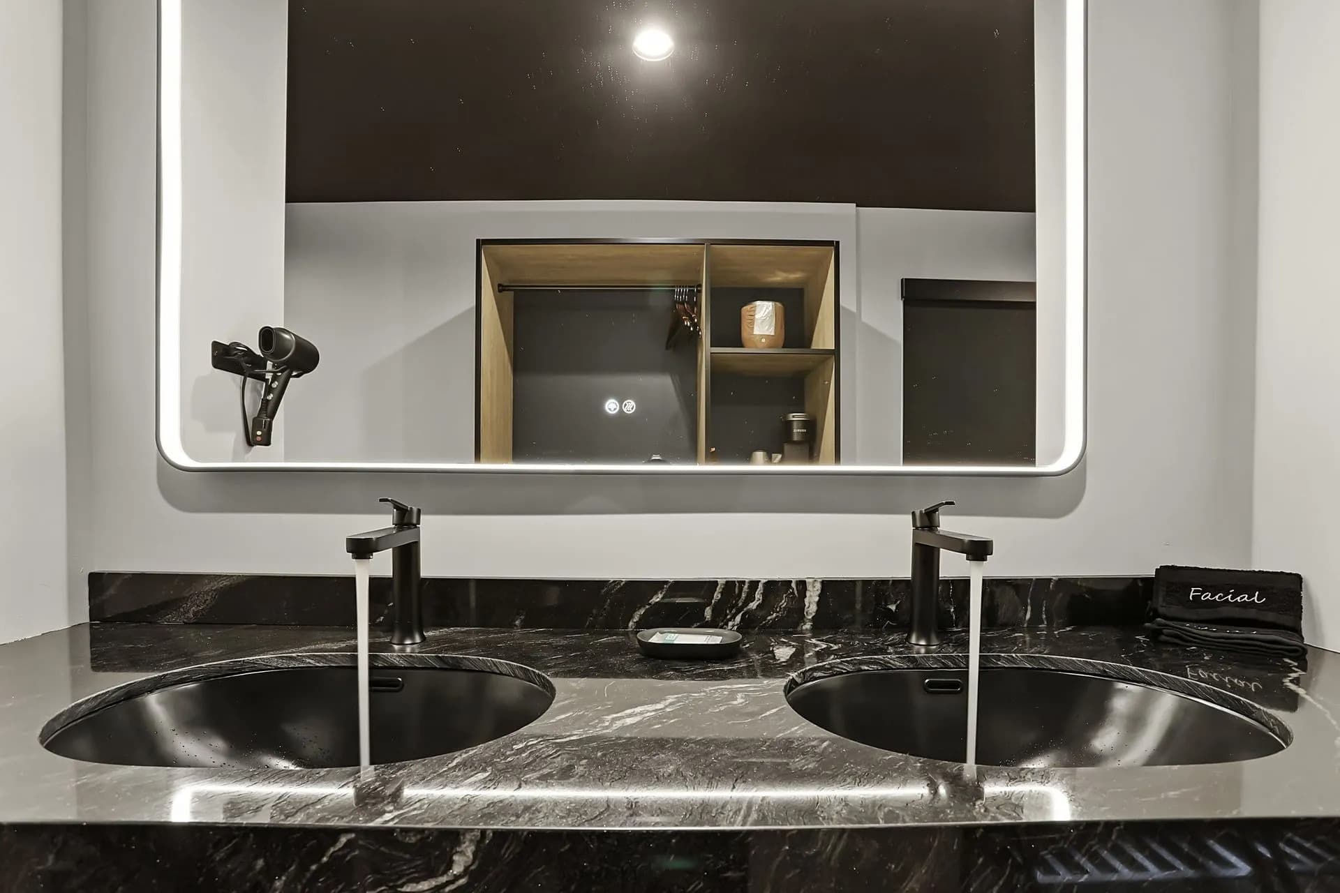 A modern bathroom sink with two circular basins, featuring sleek faucets and a mirror above, alongside a shelf displaying decor items.