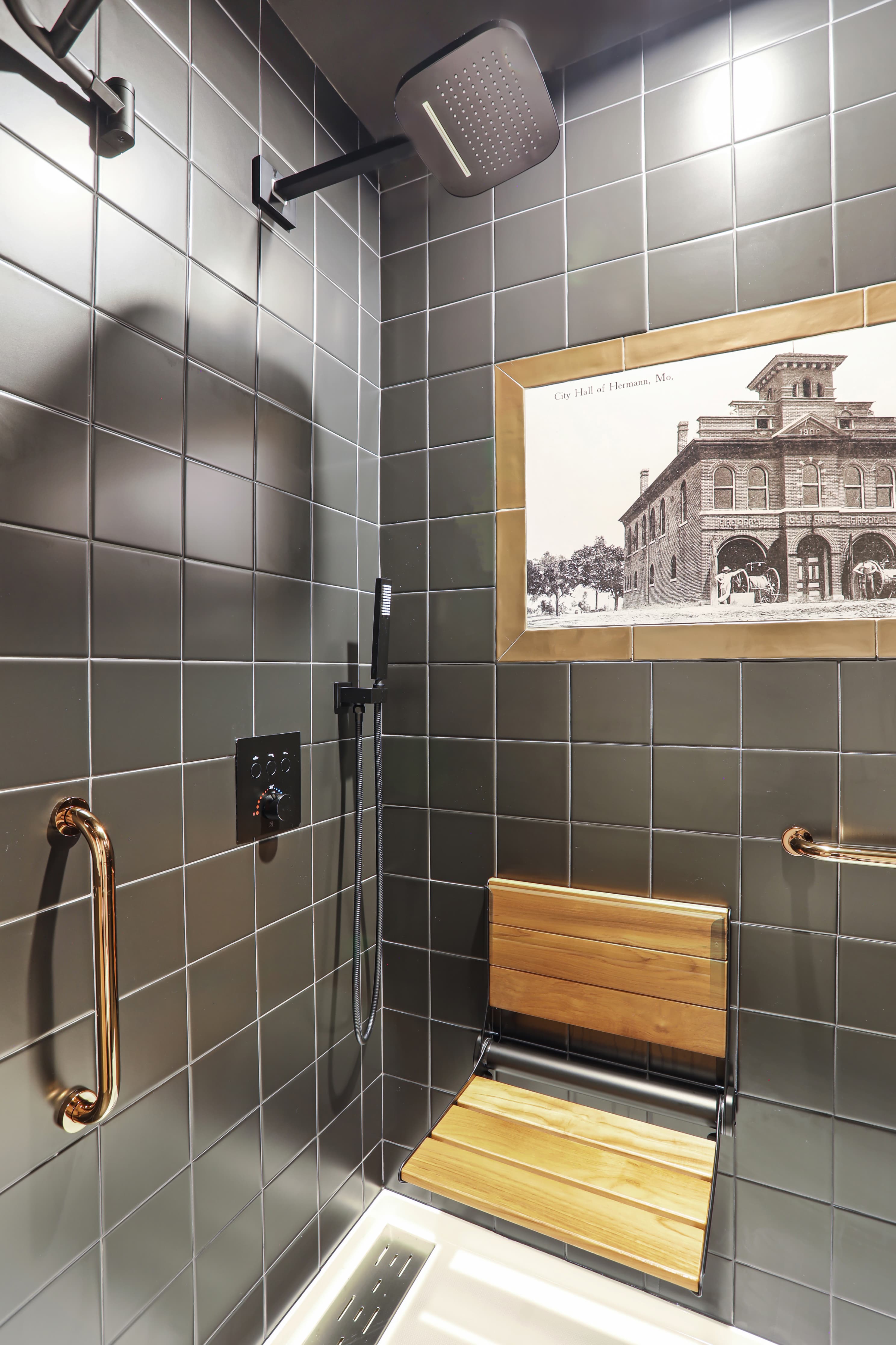 Modern shower area featuring dark tiles, a wooden bench, and a historical photograph on the wall.