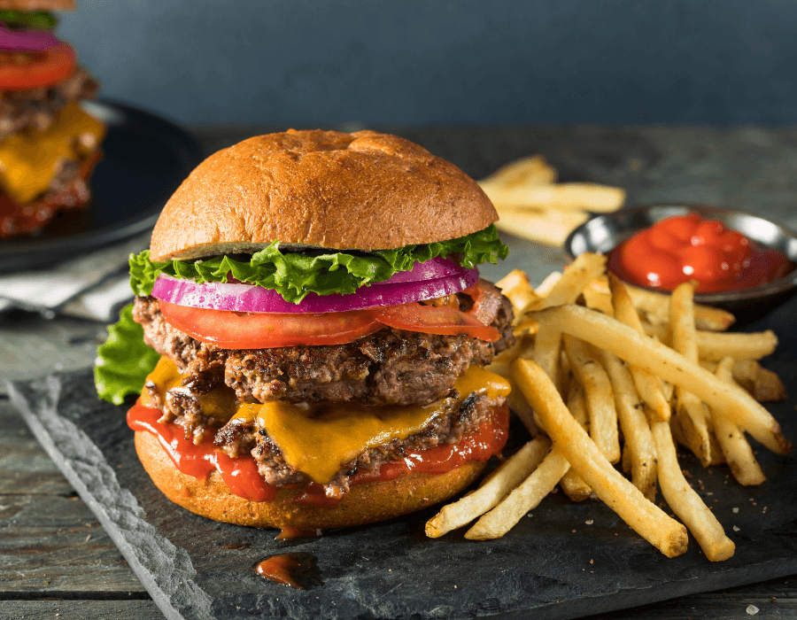 A burger with a beef patty, cheddar cheese, lettuce, tomato, and onion served with a side of fries and ketchup.