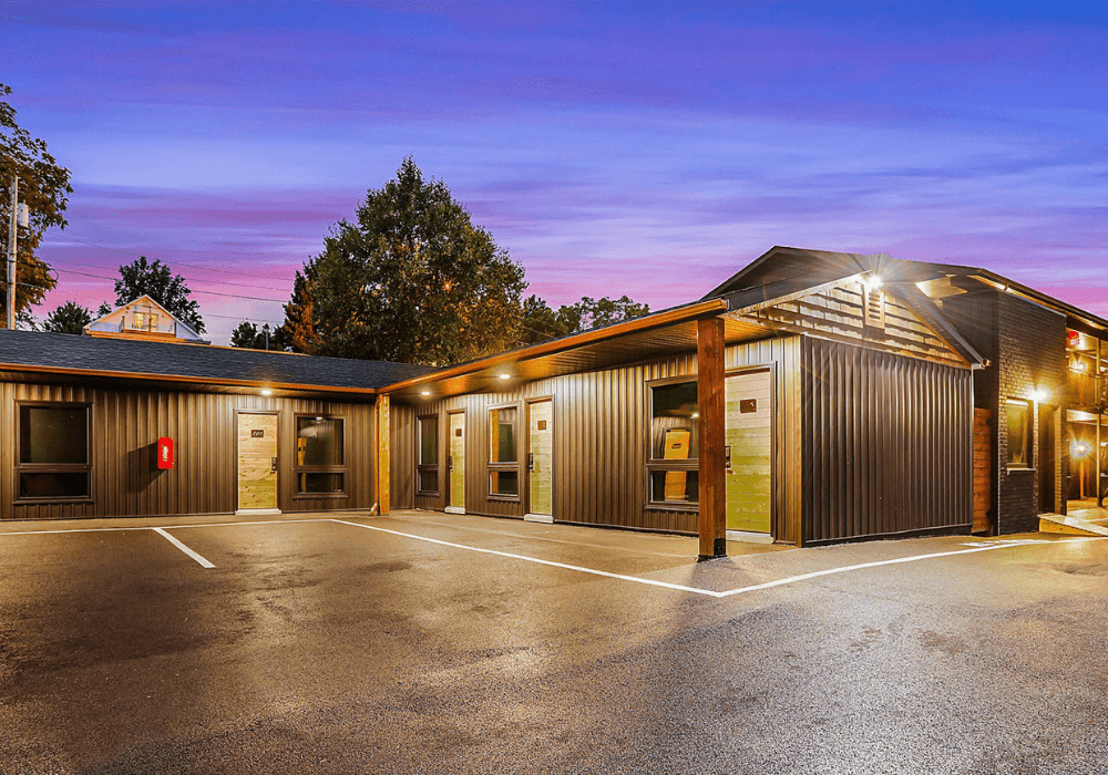Modern building exterior with a parking area at dusk, featuring warm lighting and a colorful sky.