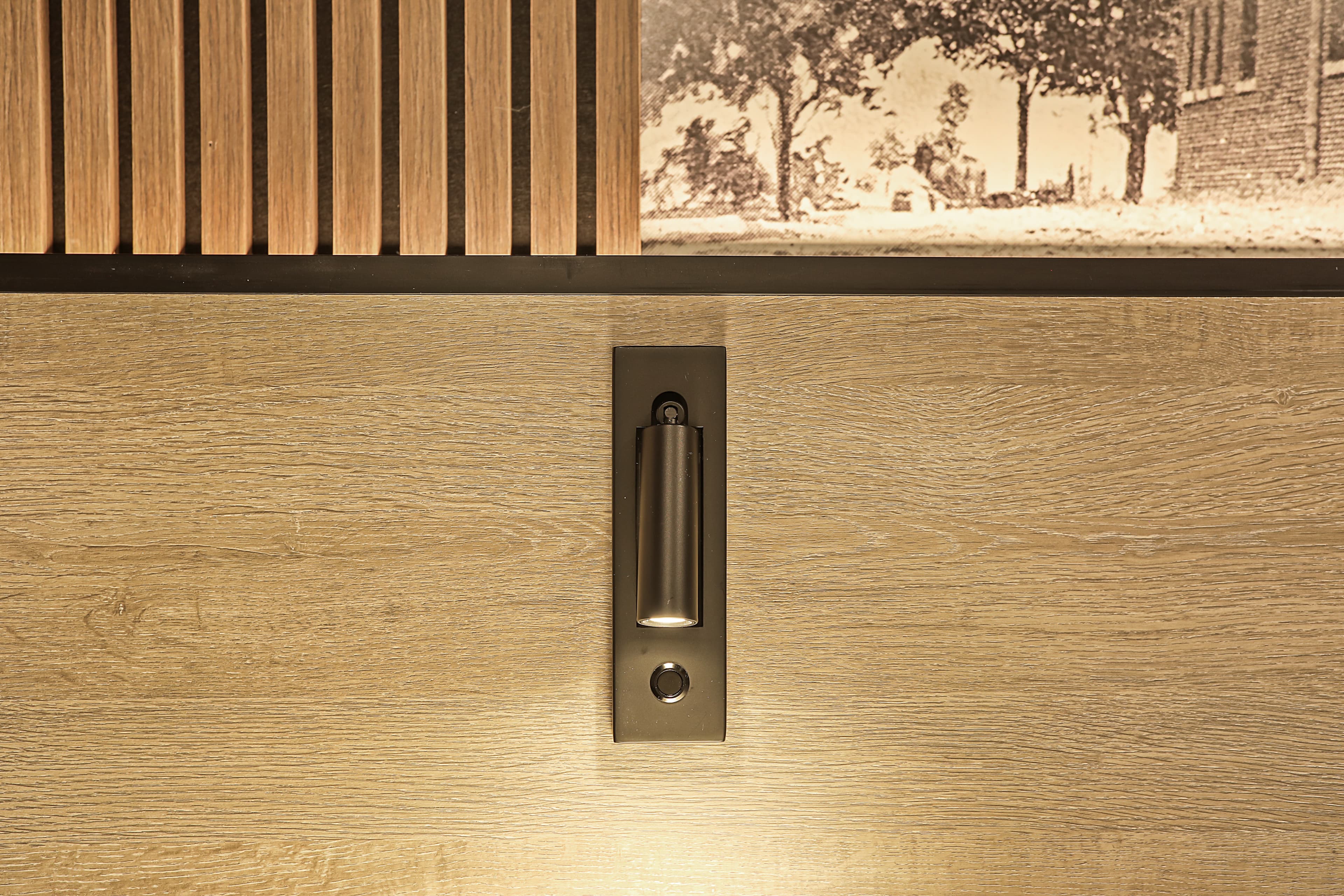 A modern wall sconce mounted on a wooden panel above a vintage photograph.