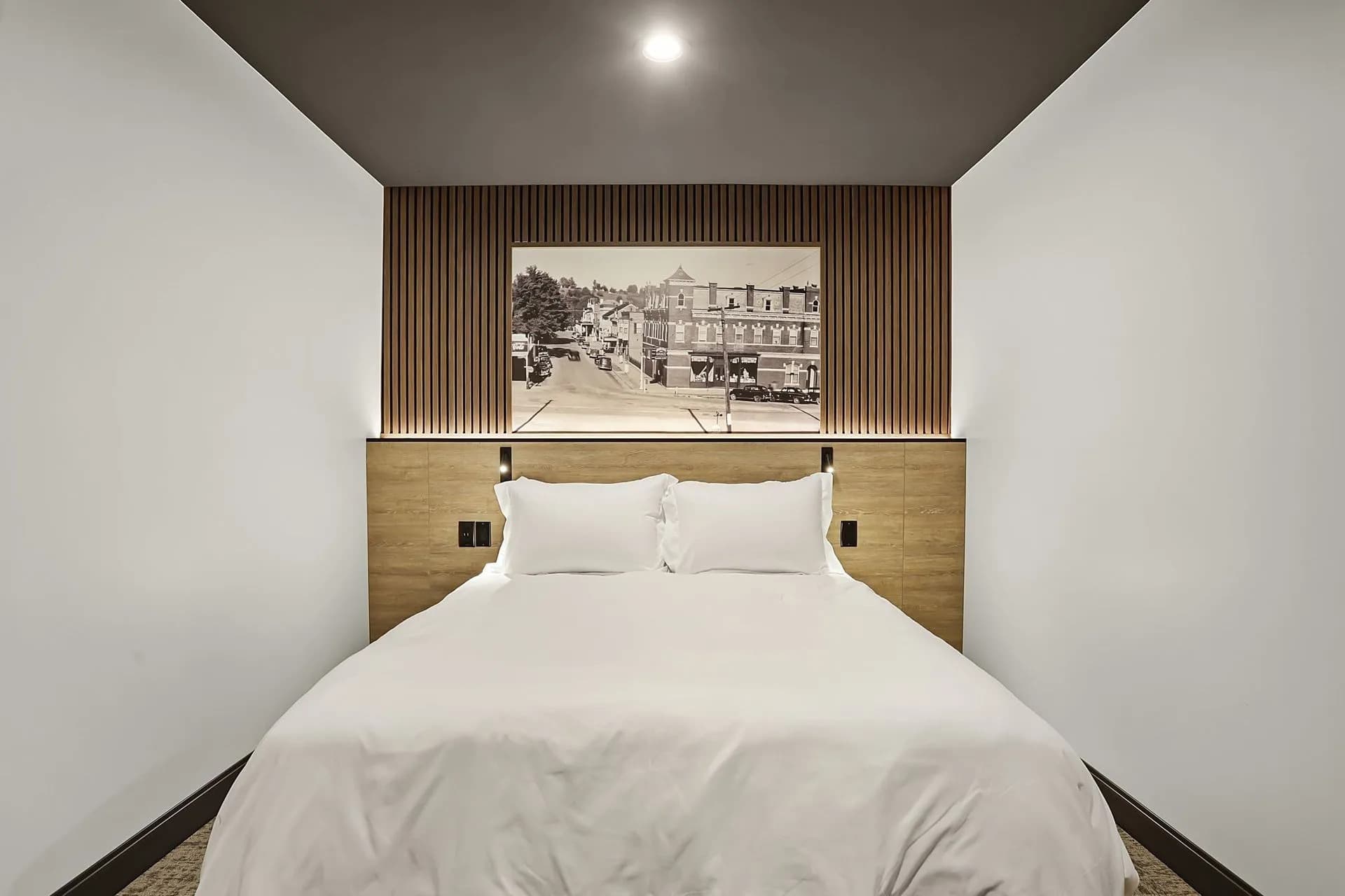 A modern hotel room featuring a double bed and a vintage-style photograph on the wall.