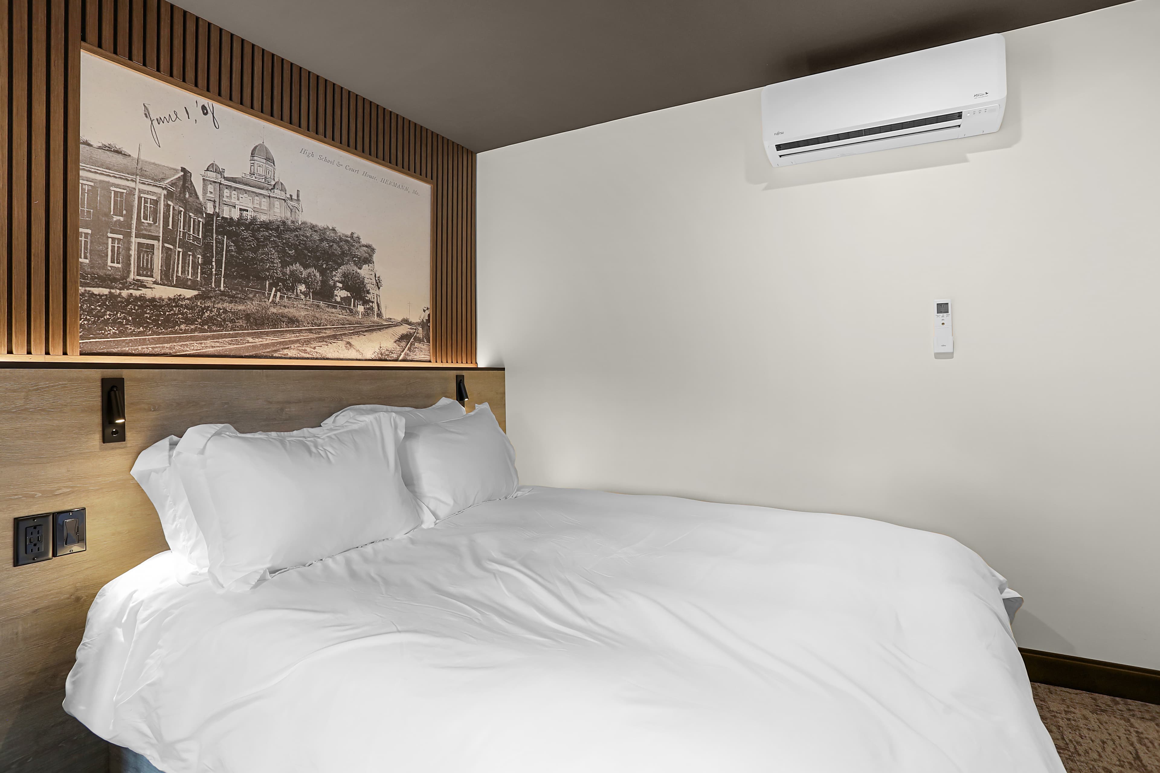 A modern hotel room featuring a neatly made white bed and a historical photograph on the wall.