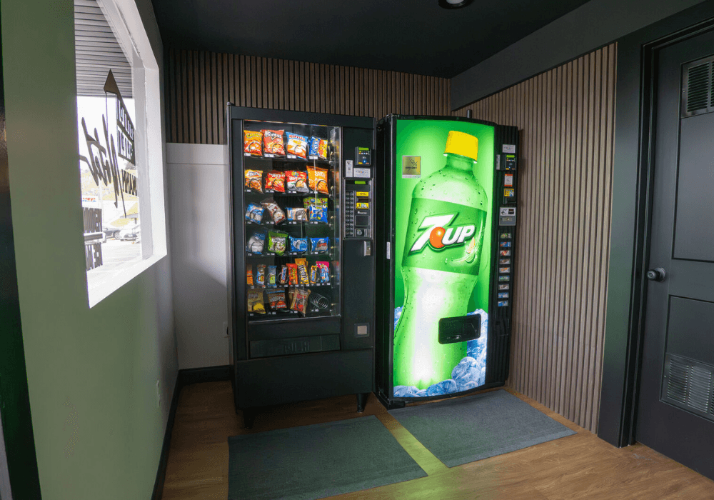 A snack vending machine and a 7UP vending machine are placed against a wall in a modern interior.