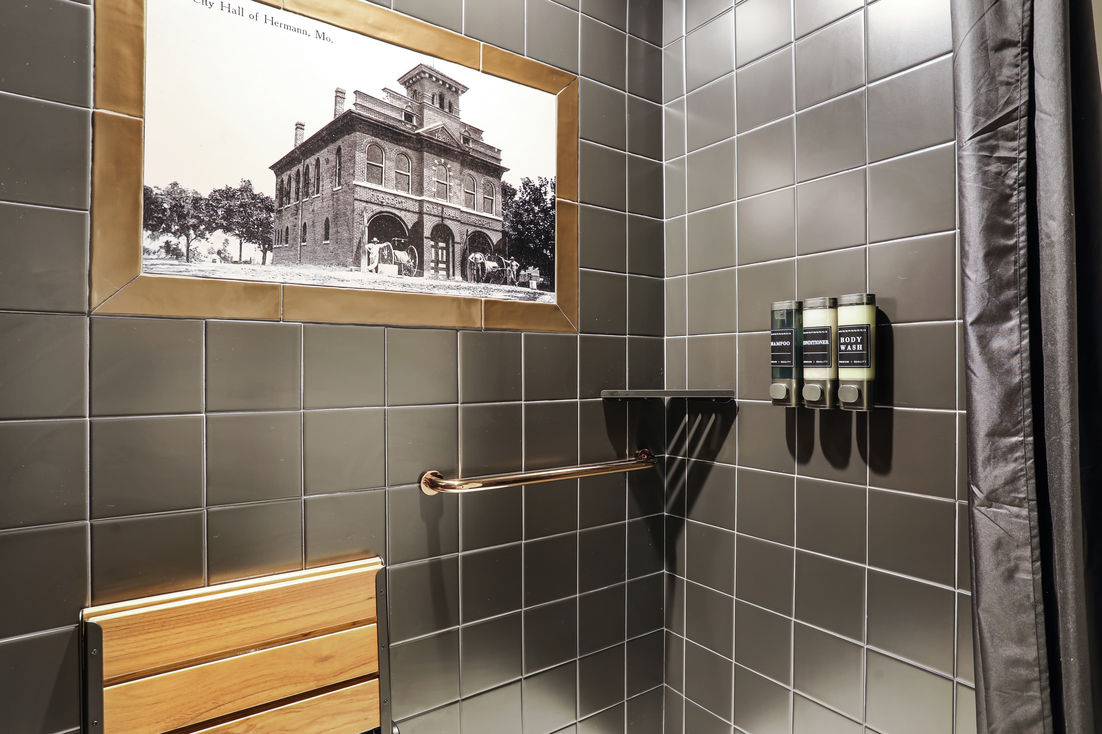 Modern shower area featuring gray tiles, a wooden bench, a vintage photo, and toiletries.