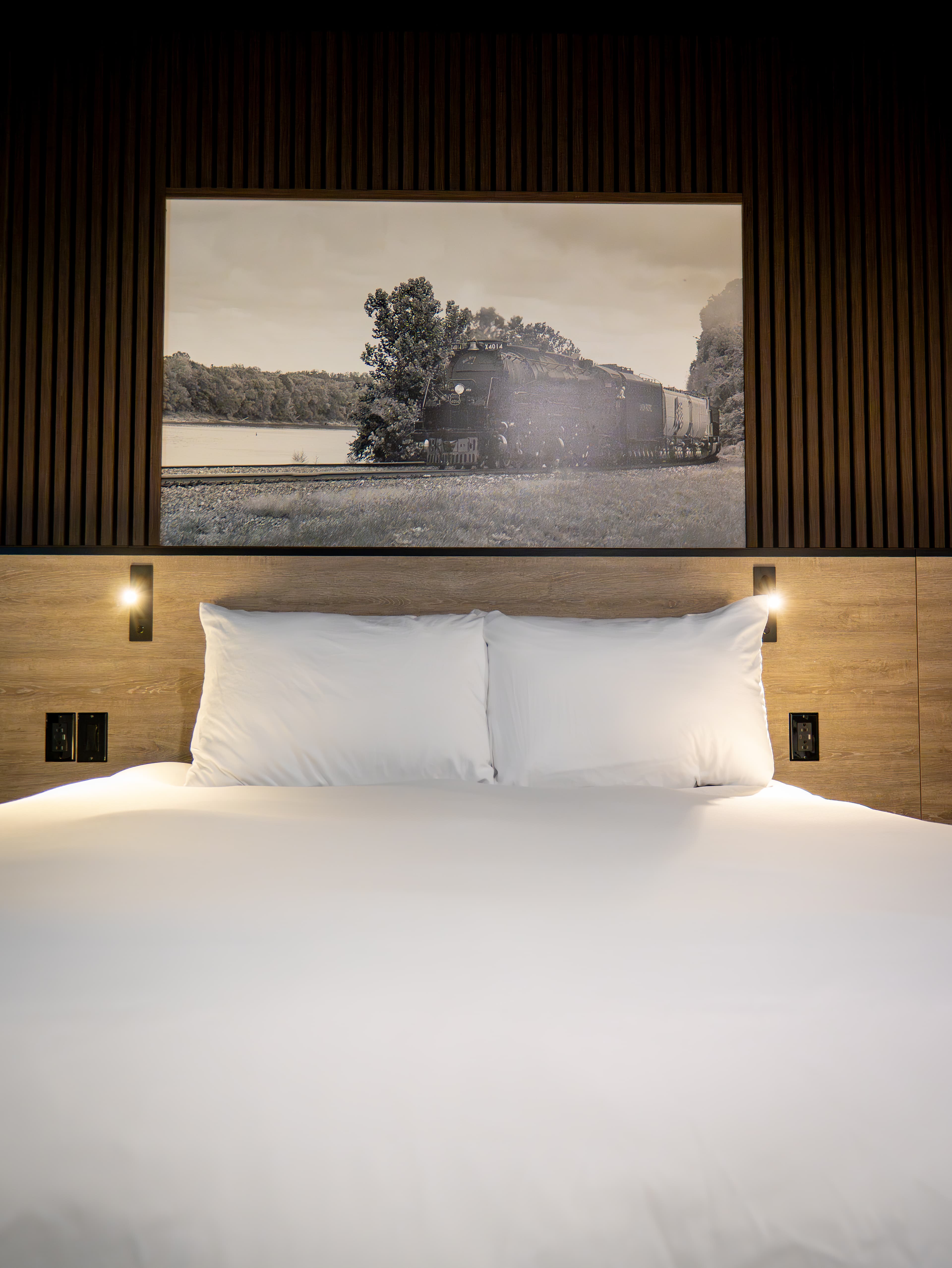 A cozy hotel bed with white pillows and a vintage train photograph on the wall above.