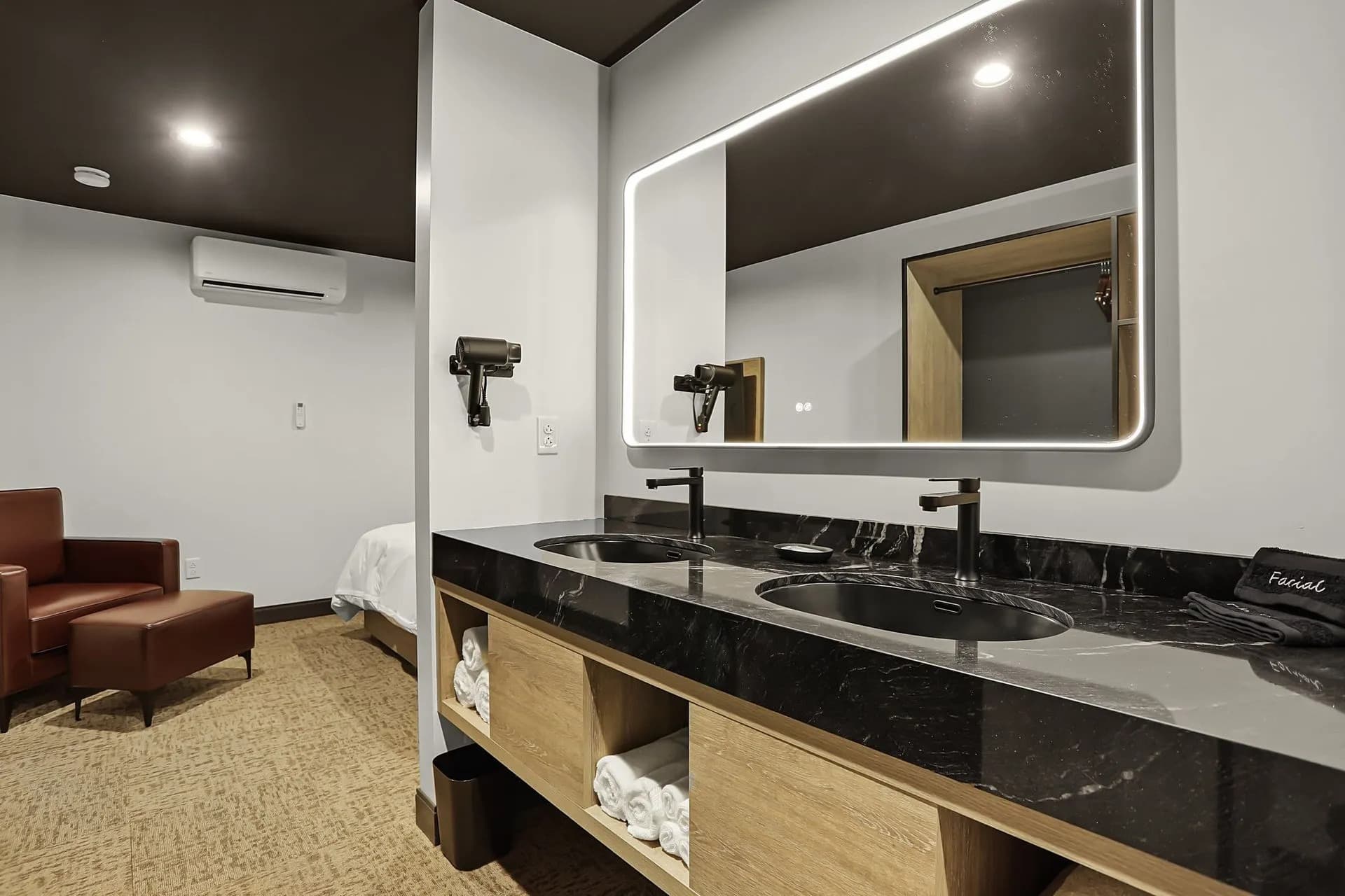 A modern bathroom featuring a double sink, backlit mirror, and wooden cabinetry with towels.