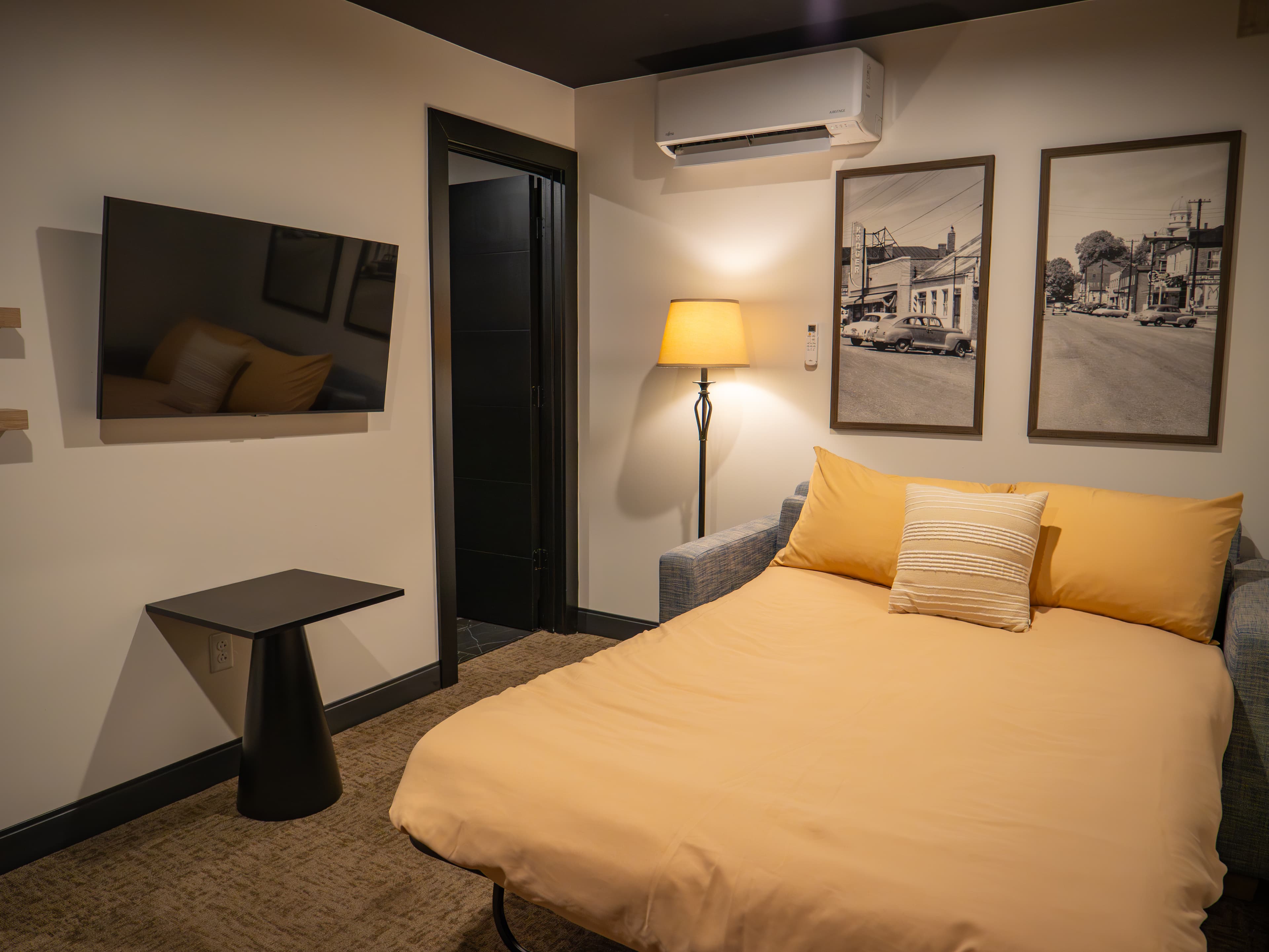 Cozy bedroom featuring a fold-out bed, lamp, TV, and framed photographs on the wall.
