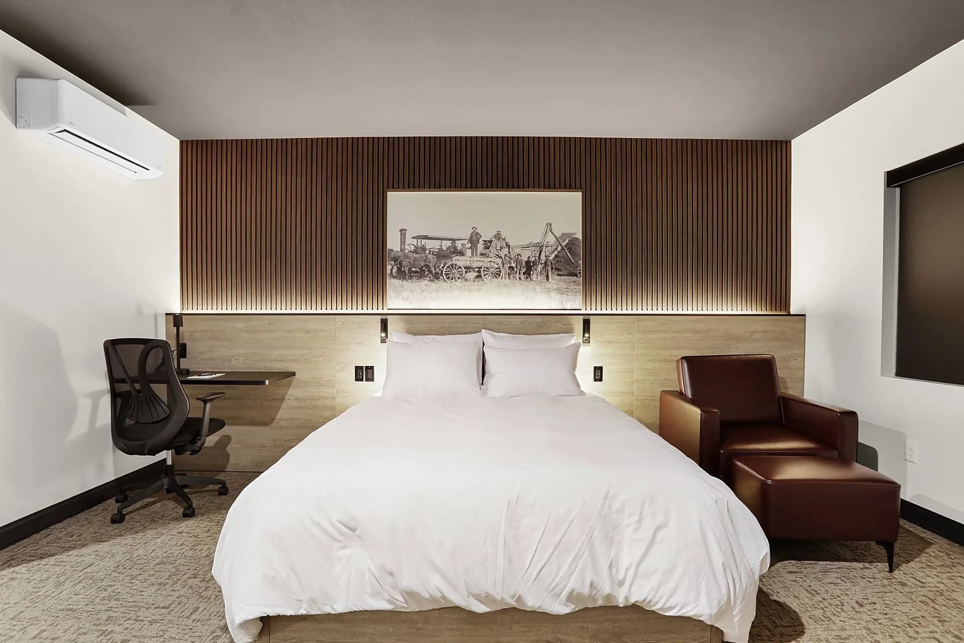 A modern hotel room featuring a queen bed, a chair, a desk, and decorative wood paneling.
