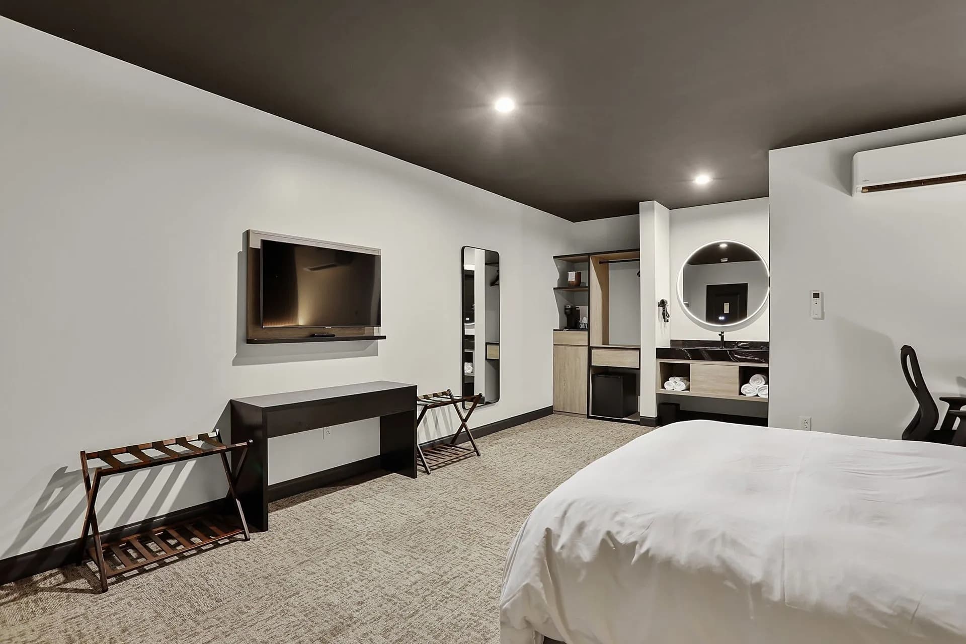 A modern hotel room featuring a bed, flat-screen TV, mirror, and kitchenette area.